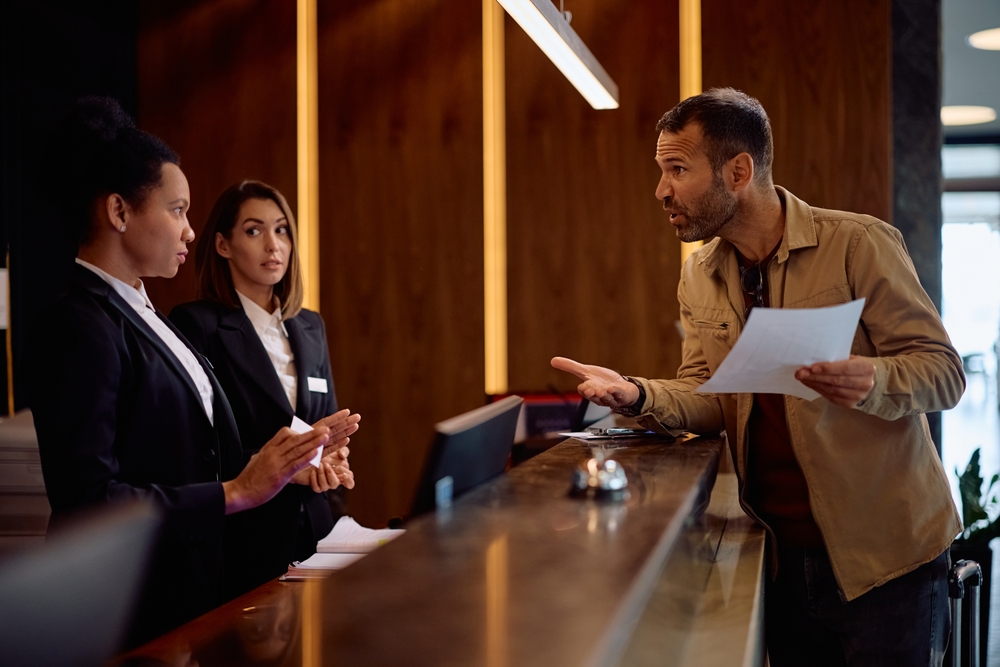 Angry guest ,trying to sue a hotel for negligence, arguing with hotel reception managers complaining about the service,